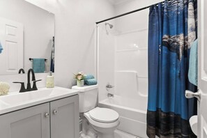 Een badkamer met een wit wastafel, een toilet, een douche en een blauw douchegordijn.
