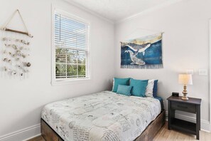 Ein Schlafzimmer mit Bett, Nachttisch, Lampe, einem Fenster mit Jalousien und einer Wanddekoration.