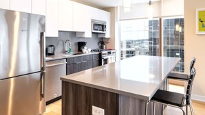 A modern kitchen with stainless steel appliances, a central island, and a view of the city through large windows.