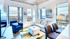Un salon moderne avec de grandes fenêtres, un fauteuil bleu, un canapé blanc et une table basse.