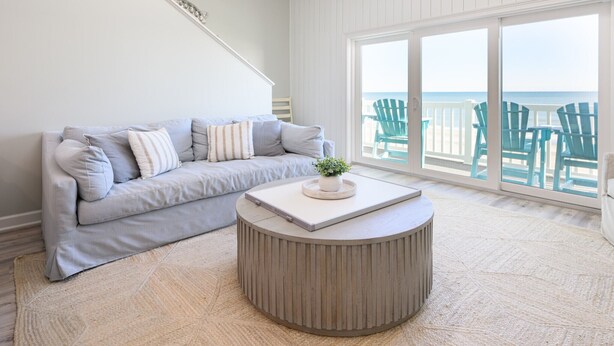 Ein Wohnzimmer mit einem hellgrauen Sofa, einem runden Couchtisch und Meerblick durch große Fenster.