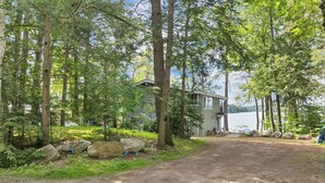 A cabin with a dirt path leading to it, surrounded by trees and a lake.