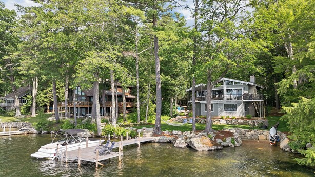 A lakeside property with a dock, a house with a large deck, and a stone pathway leading to the water.