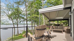 A deck with Adirondack chairs and a sofa overlooking a lake.