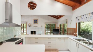 A modern kitchen with white cabinetry, a built-in stove, and a large window offering a view of greenery. - Time and Tide in Inverloch (Inverloch)