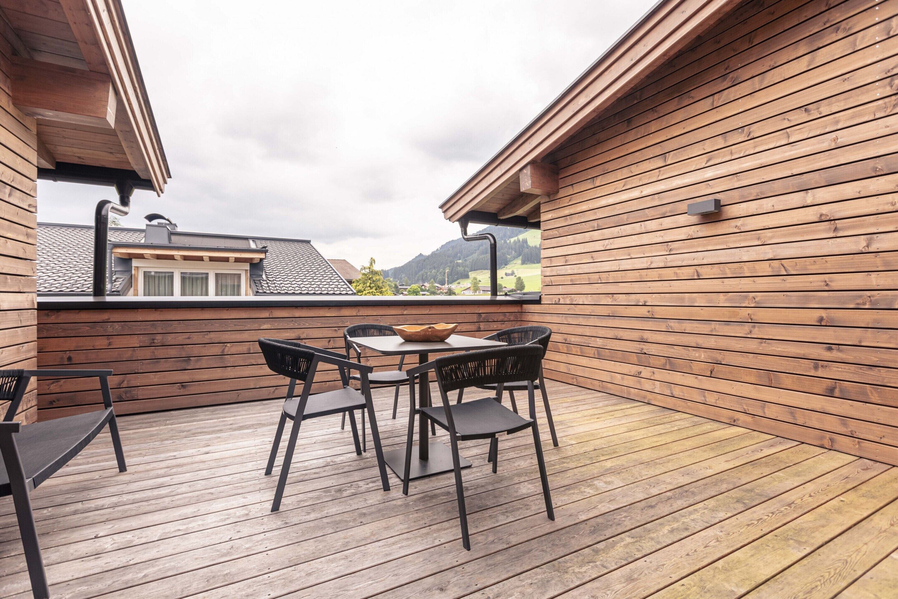 A wooden deck with a table and chairs, overlooking a mountainous landscape.