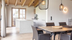A modern kitchen with wooden beams, a dining area with a table and chairs, and a view of the outside through large windows. - Penthouse in Tyrol With Infrared Sauna (Westendorf)