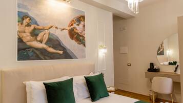 Habitación de hotel con una cama grande, almohadas verdes, un cuadro en la pared, un escritorio con una silla y una araña.