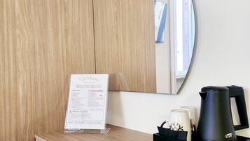 A hotel room with a wooden desk, a black tray with a coffee maker, a mirror, and a welcome sign.
