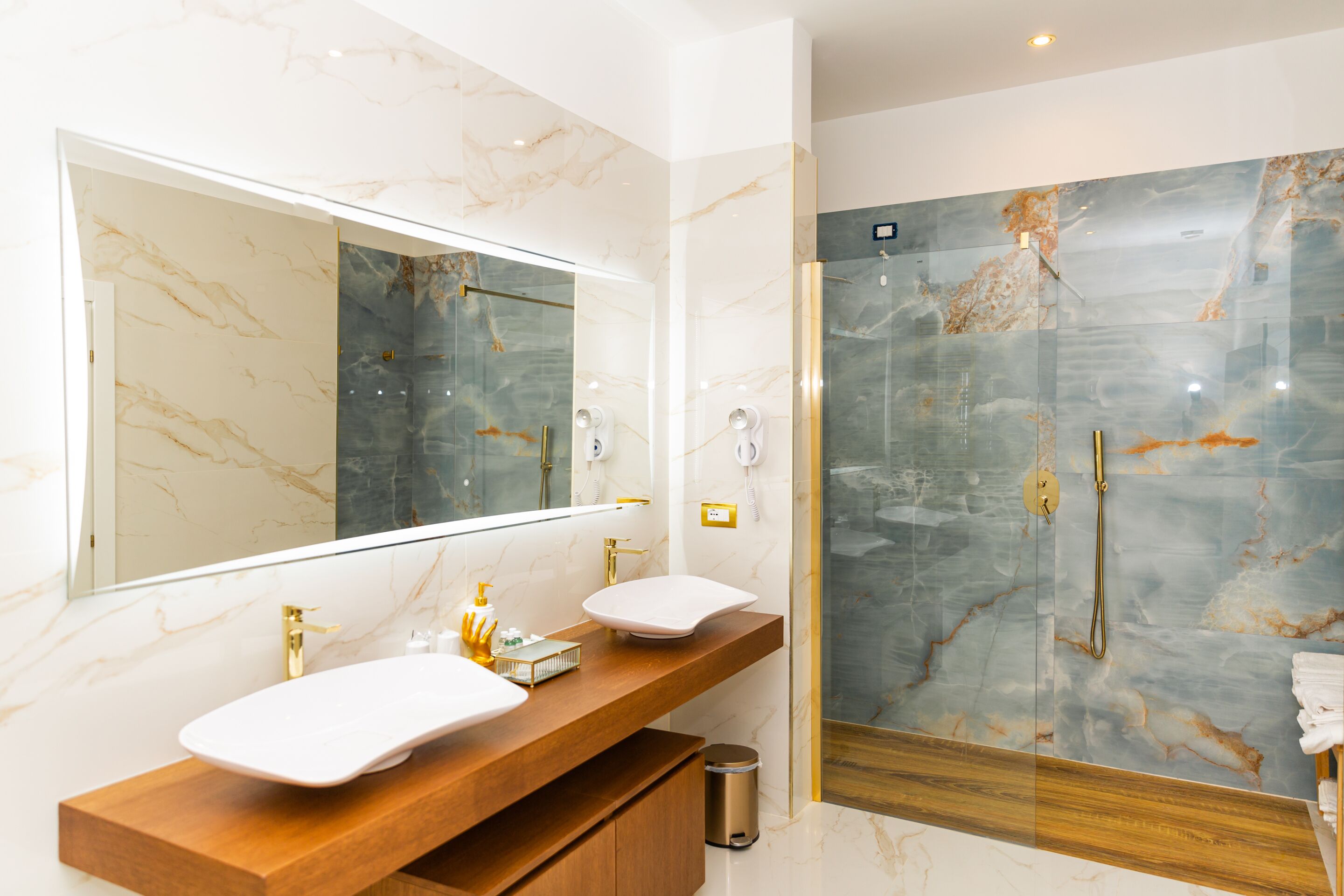 Une salle de bain moderne avec un grand miroir, deux lavabos, un espace douche et des murs en marbre.