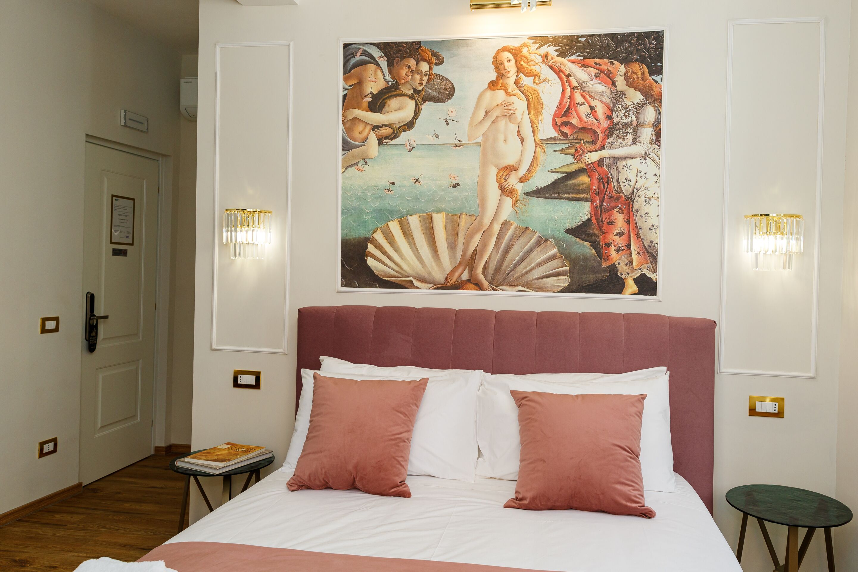 A bedroom with a large bed, a painting on the wall, and two wall sconces.