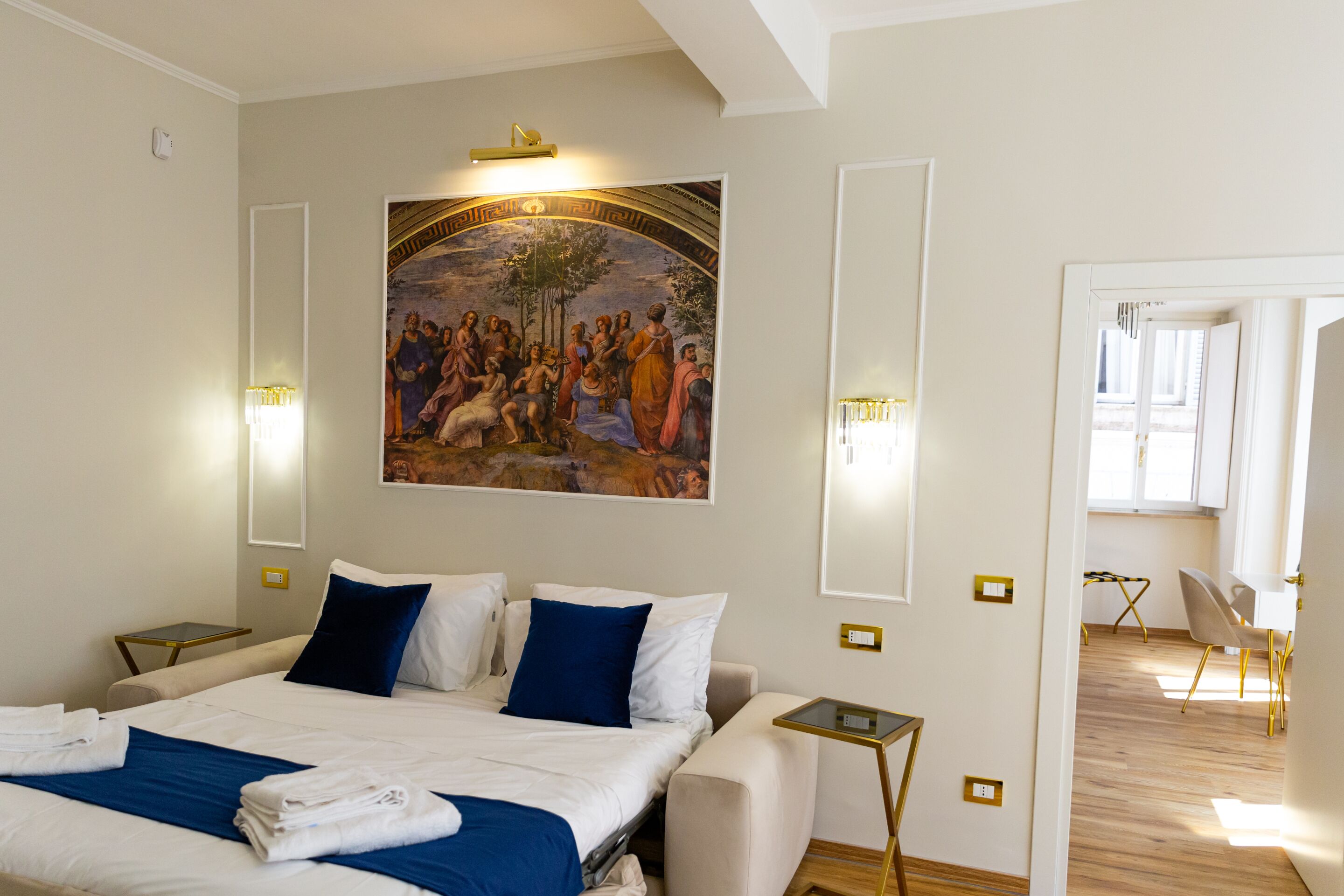 A hotel room with a large bed, two bedside tables, a painting on the wall, and a view of the adjacent room.