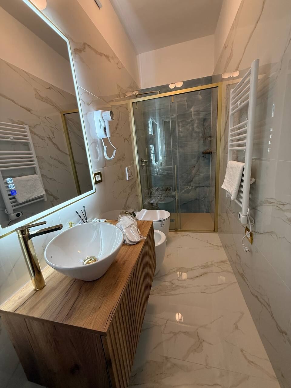 A modern bathroom with a wooden vanity, a large mirror, a glass shower enclosure, and a white toilet.