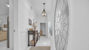 A hallway with a white marble floor, a textured rug, a wicker side table with a lamp, and a decorative glass door.
