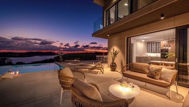 Ein moderner Außenbereich mit Pool, Sitzgelegenheiten und Blick auf den Sonnenuntergang über dem Wasser.