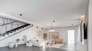 Ein modernes Wohnzimmer mit Treppe, weißen Sofas, einem Couchtisch und einem großen Gemälde an der Wand.