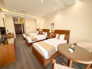 A hotel room with three beds, a desk, and a round table. - north paradise hotel (Irbid)