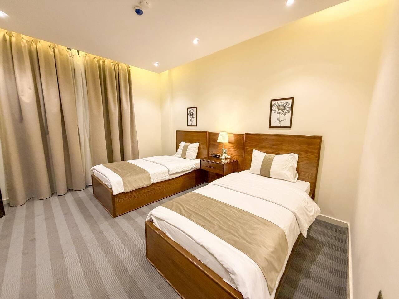 A hotel room with two beds, a nightstand, a lamp, and a window with curtains.