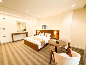A hotel room with a bed, bedside tables, a round table, and a chair.