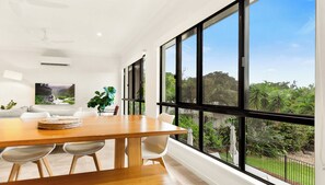 Un comedor moderno con una mesa de madera, sillas blancas y un amplio ventanal con vistas a abundante vegetación.