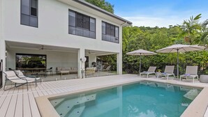 Una casa moderna de dos pisos con piscina, mobiliario exterior y zona de patio.