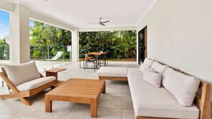 Un espacio exterior moderno con un sofá, dos mesas de madera y una mesa de comedor con sillas.