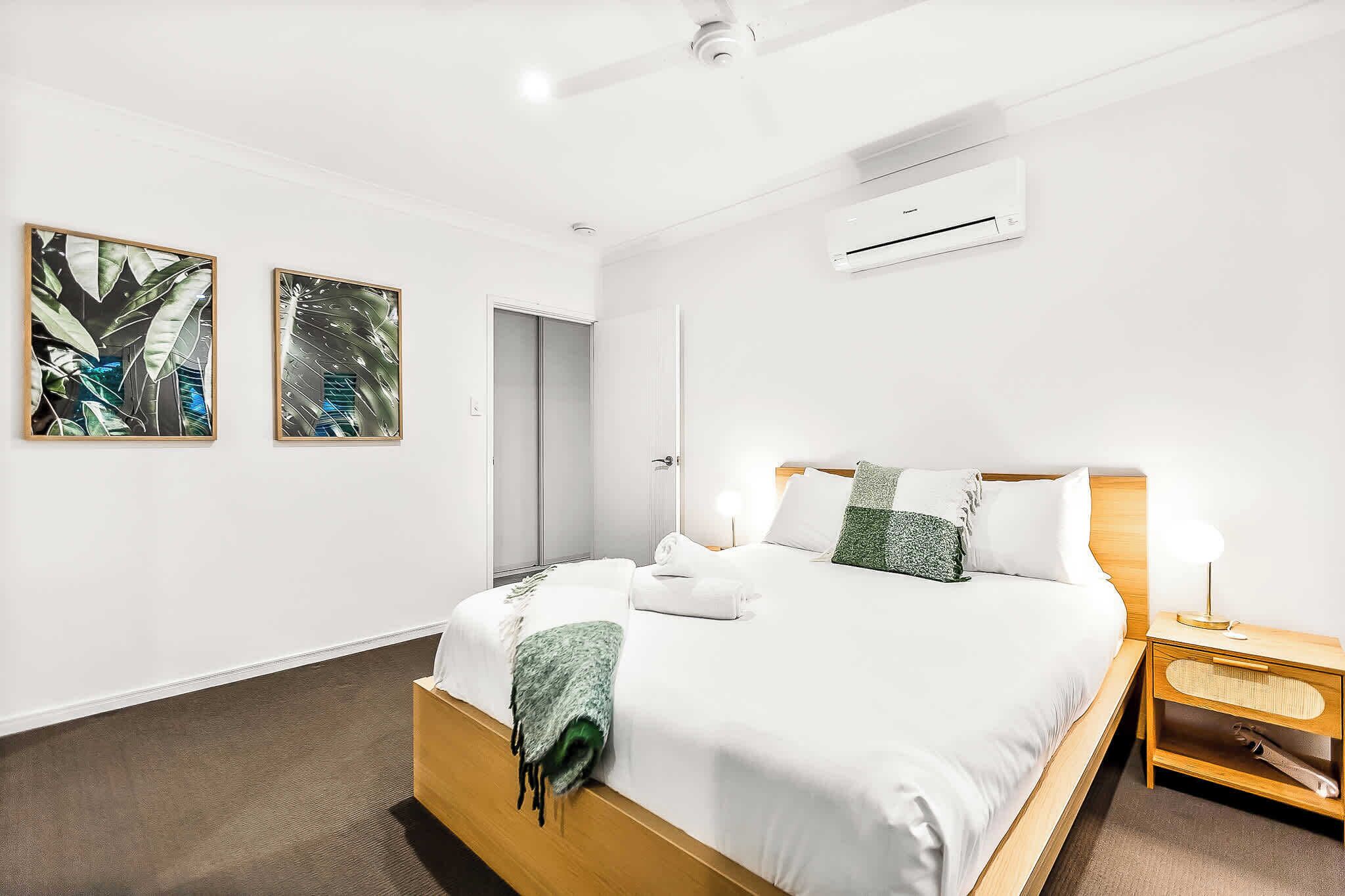 A hotel room with a bed, bedside table, and two wall-mounted air conditioning units.
