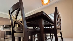 A dining area with a dark wooden table and chairs, a hanging pendant light, and a kitchen in the background. - Country Space Villa (Gated Community, private pool, close to turtle watching) (Sangre Grande)