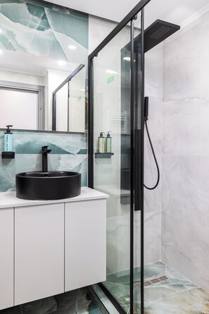 A modern bathroom with a glass-enclosed shower, a black sink, and marble-like wall tiles. - Ophelia Suites by halu! (Thessaloniki)