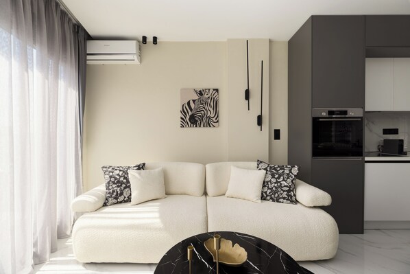 A modern living room with a sectional sofa, a black and white zebra artwork, and a kitchen area with a built-in oven. - Ophelia Suites by halu! (Thessaloniki)