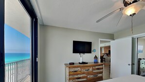 Een slaapkamer met een groot bed, een dressoir, een televisie en een balkon met uitzicht op zee.
