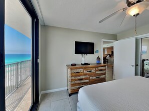 Un dormitorio con una cama grande, un aparador, un televisor y un balcón con vista al océano.