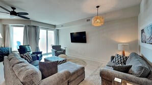 A modern living room with a sofa set, a patterned armchair, a ceiling fan, a TV, and a pendant light.