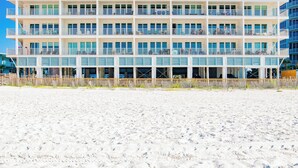 A multi-story hotel with balconies, located on a sandy beach.