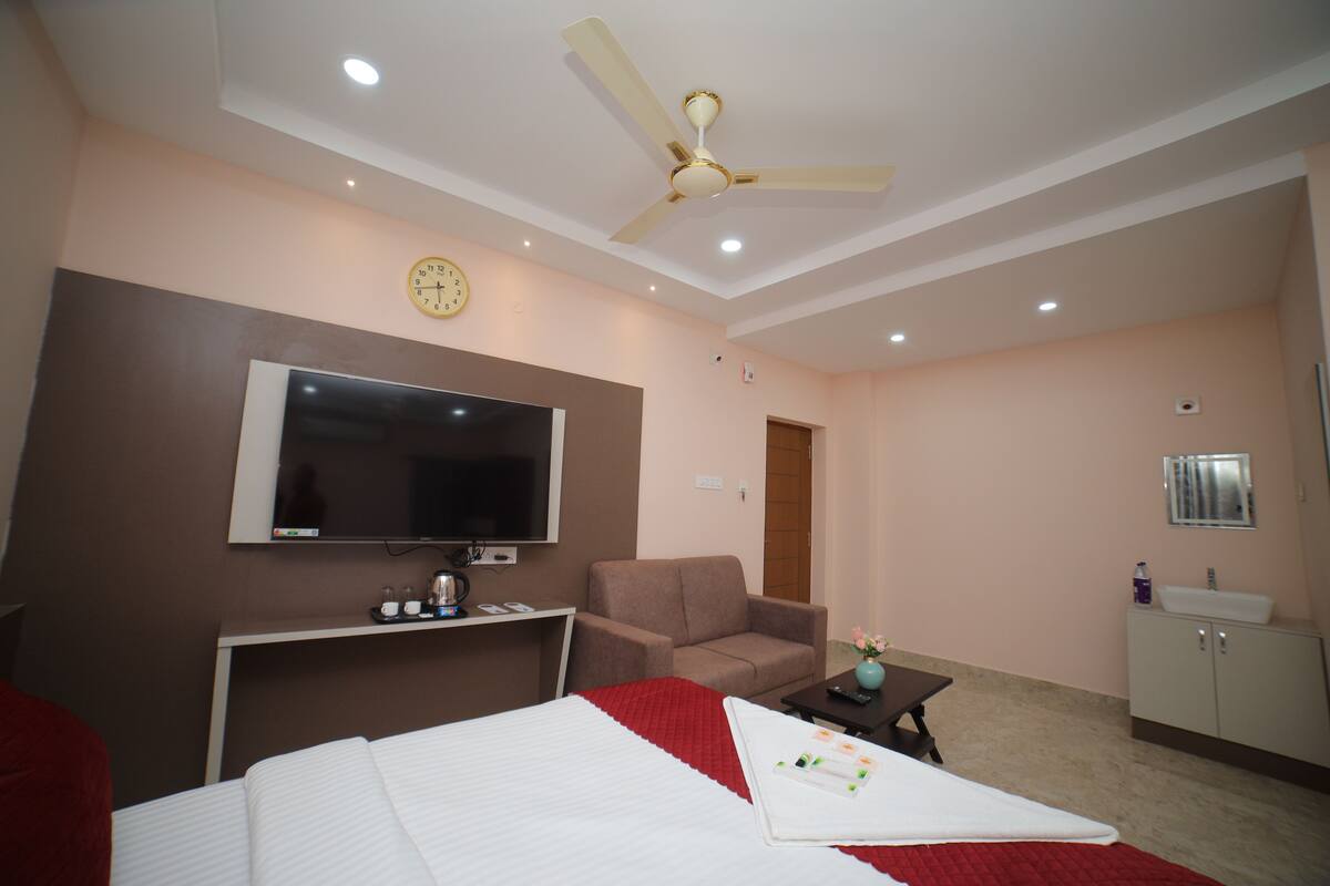 A hotel room with a bed, a TV, a ceiling fan, a desk, a chair, and a bathroom.