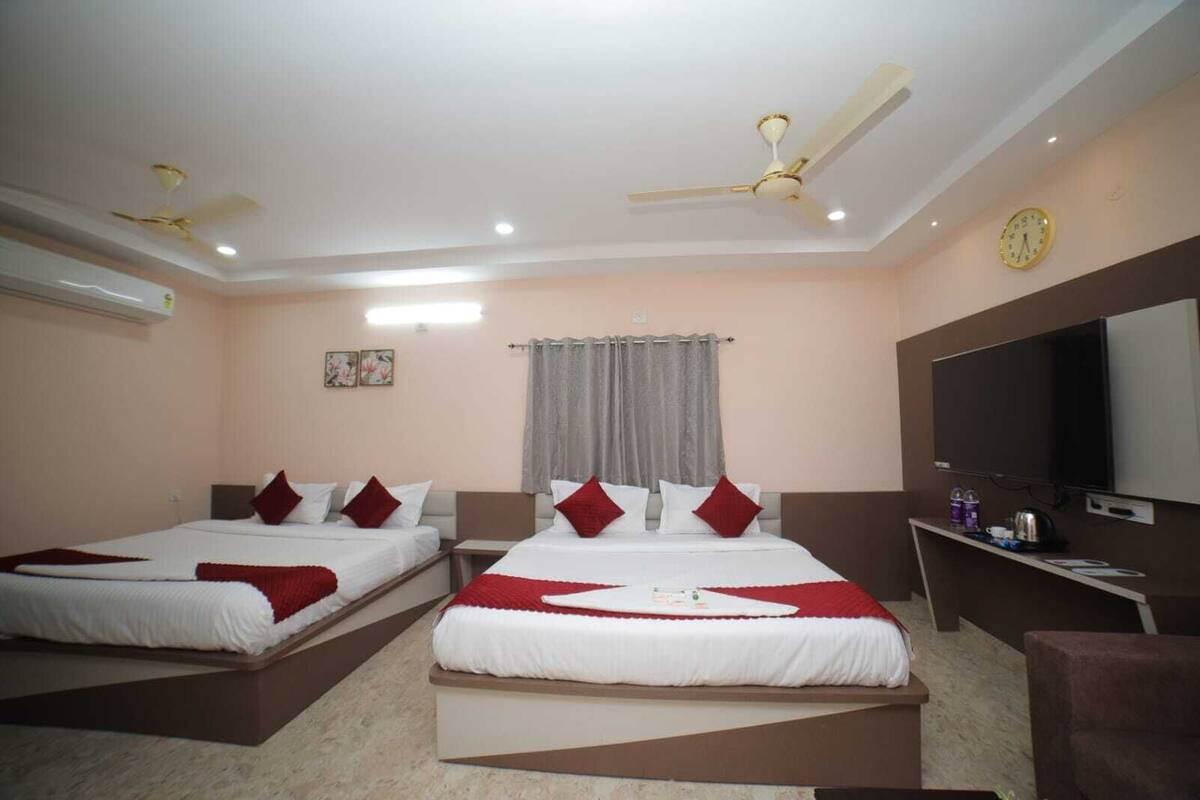 A hotel room with two beds, a TV, a clock, and a ceiling fan.