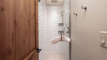 A shower area with white tiled walls, a wooden door, and a towel hanging on a rack.