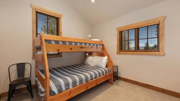 A bunk bed with a wooden frame, a striped bedspread, and a chair. There are two windows with wooden frames and blinds.