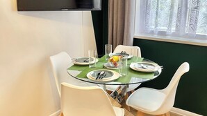A dining area with a glass table, white chairs, and a flat-screen TV mounted on the wall. - The Express Apartment (Ilford)