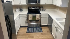 Eine moderne Küche mit weißen Schränken, einem Edelstahlkühlschrank, einer Mikrowelle, einem Backofen und einem Spülbecken.