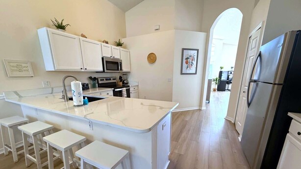 A modern kitchen with white cabinetry, a central island with stools, stainless steel appliances, and a view to the dining area. - 4 Bedroom Villa with Private Pool & Golf Course Views (Haines City)