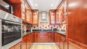 A kitchen with wooden cabinets, a stainless steel oven, a microwave, and a tiled backsplash. - Cozy 1BR Apartment | Close to Mall, Metro, and Dining (Dubai)
