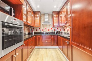 Eine Küche mit Holzausstattung, einem Edelstahlbackofen, einer Mikrowelle und einer gefliesten Spritzschutzwand.