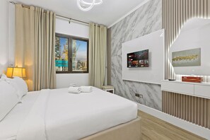 Une chambre d’hôtel avec un lit, une télévision, une fenêtre donnant sur la ville, une lampe et un tableau au mur.
