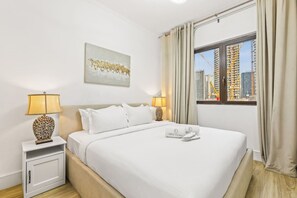 Ein Hotelzimmer mit Bett, zwei Nachttischlampen, einem Fenster mit Vorhängen, Blick auf die Stadt und einem Bild an der Wand.