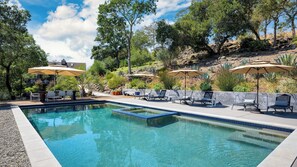 A rectangular swimming pool with clear blue water, surrounded by a deck area with lounge chairs and umbrellas.