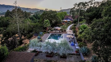 Una piscina con tumbonas y sombrillas alrededor, rodeada de jardines y árboles.