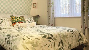 A bedroom with a checkered wall, a bed with leaf-patterned bedding, a bedside lamp, and a window with leaf-patterned curtains. - Norwich Delight Apartment (Romford)