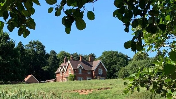 A house by a clear stream with surrounding greenery.