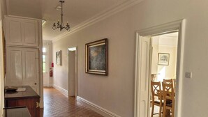 A spacious hallway with wooden flooring, white walls, and a dining area visible through an open door.
